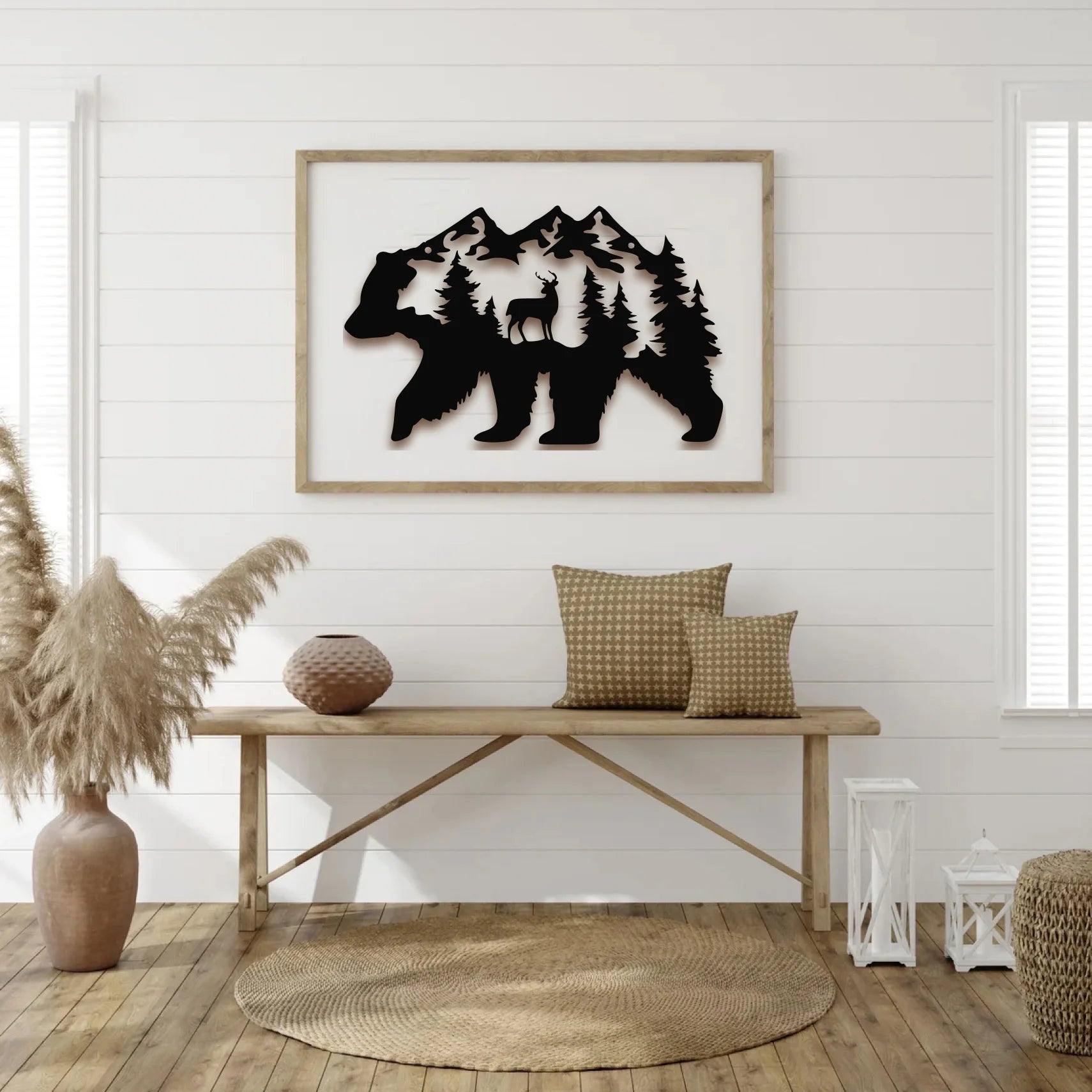 Framed metal wall art of a bear silhouette filled with mountains, deer, and trees, adding a rustic touch to a white shiplap living room with wooden accents.