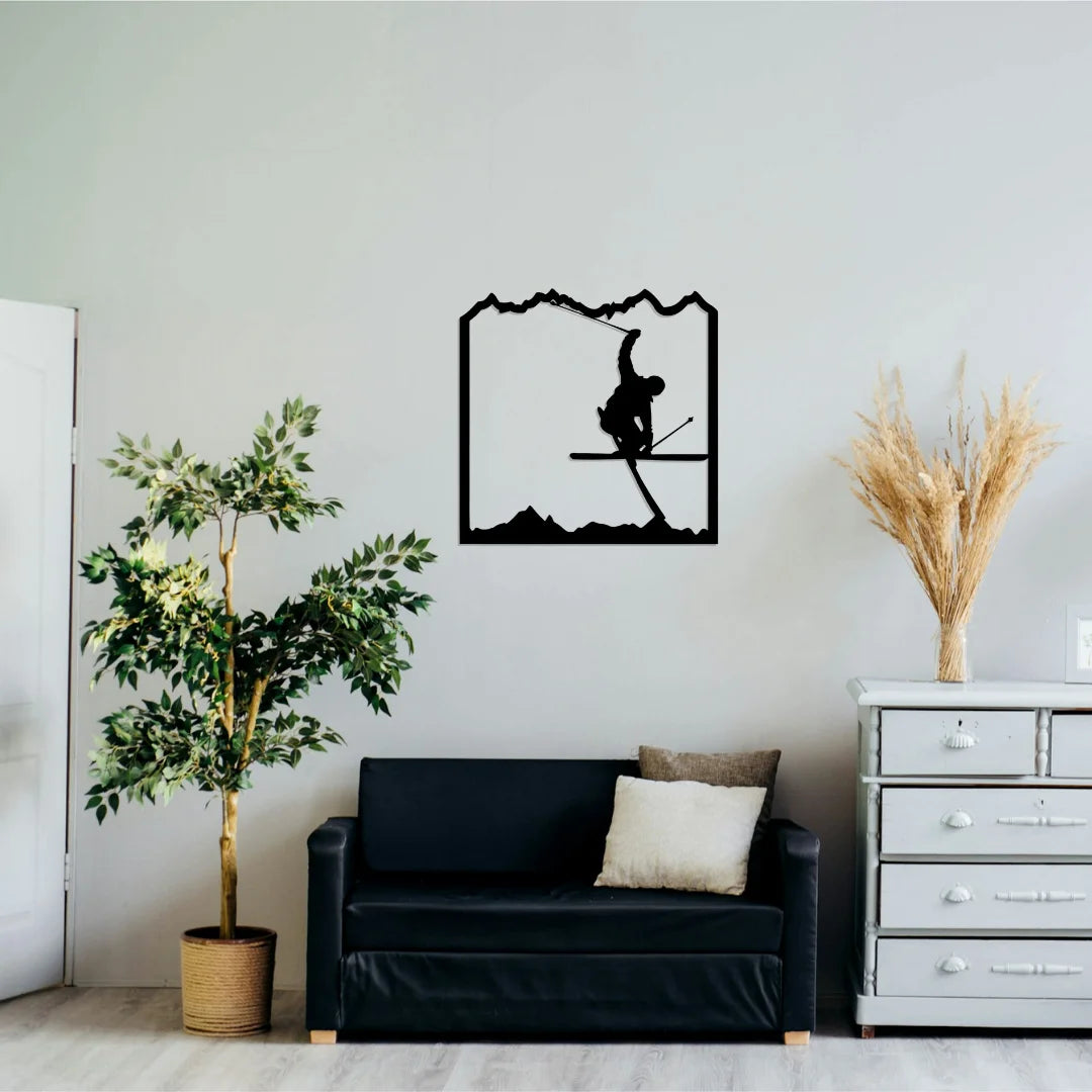 A black silhouette of a skier mid-jump framed by mountains forms a unique sports wall art decor feature, hung above a simple black couch in a minimal living room.