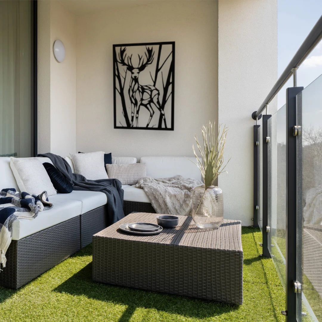 A tall metal wall hanging featuring a deer silhouette framed by trees adds a rustic charm to this cozy balcony nook.