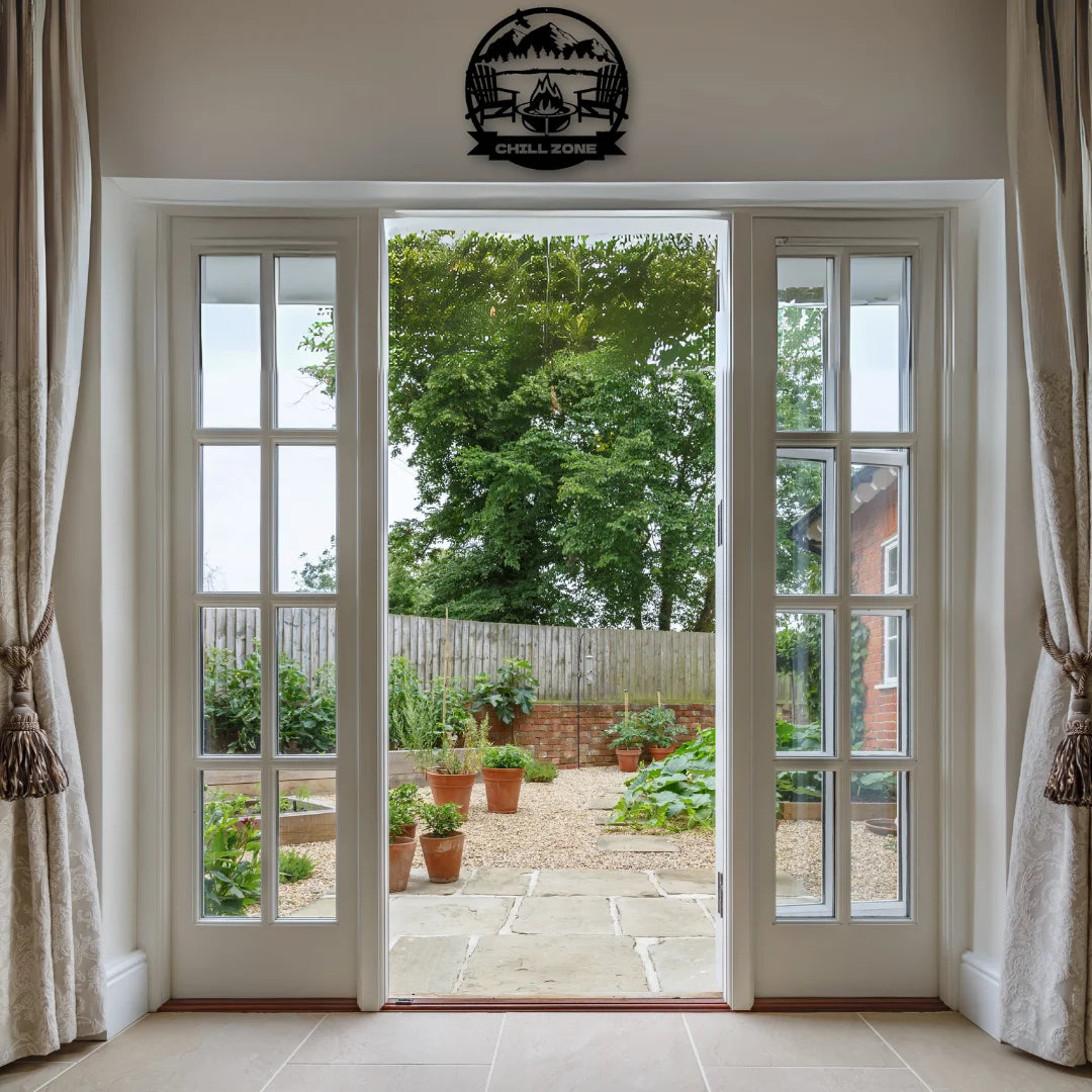 A cozy indoor view framed by French doors and topped with rustic cabin wall art reading “Chill Zone,” perfect for peaceful garden transitions.