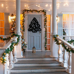 A festive porch features a Christmas tree-shaped letter a monogram sign on the door, surrounded by garlands and lights, part of welcoming christmas signs decor.