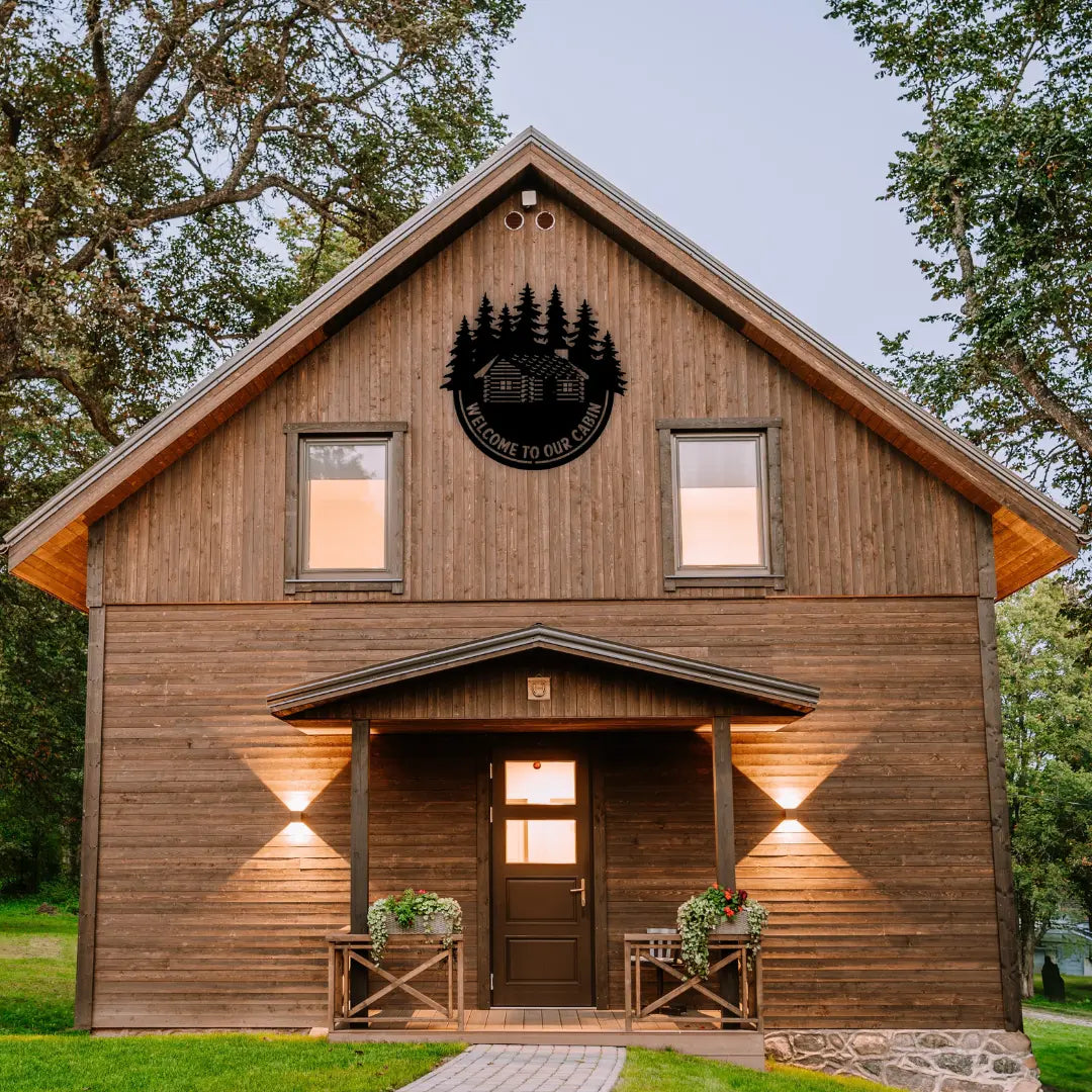 This welcome signs for lake house piece displays a cabin under pine trees and hangs proudly on a rustic cabin front, making it a favorite among cabin decorations collectors.