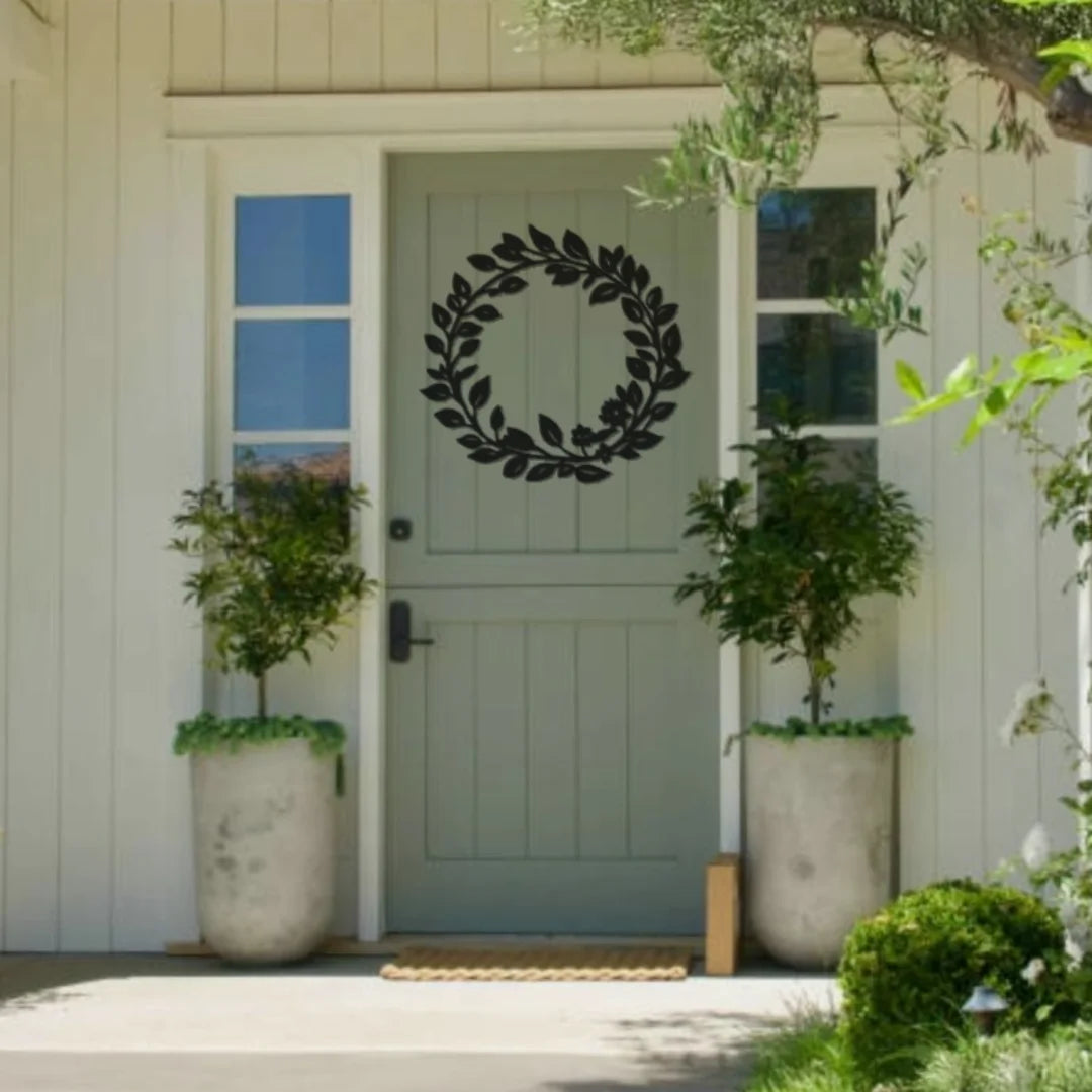 A minimalist black metal outdoor decoration in the shape of a leafy wreath is mounted on a pale green door, offering timeless elegance to a cozy front porch.
