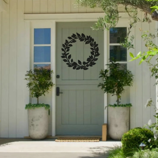 A minimalist black metal outdoor decoration in the shape of a leafy wreath is mounted on a pale green door, offering timeless elegance to a cozy front porch.
