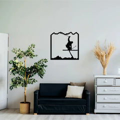 A black silhouette of a skier mid-jump framed by mountains forms a unique sports wall art decor feature, hung above a simple black couch in a minimal living room.
