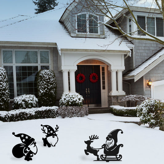 Three playful metal garden gnome decorations, including reindeer and sleigh designs, add holiday spirit to a snow-covered front lawn.
