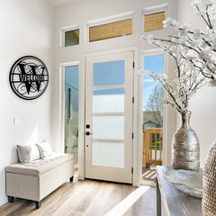 A circular black welcome sign metal with a decorative initial adds charm to a white entryway, warmly greeting guests with elegance and personality.
