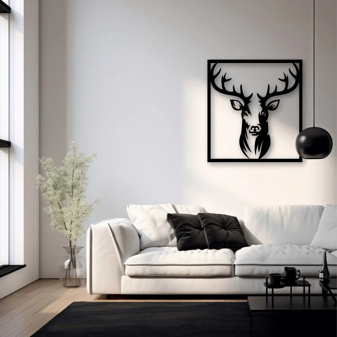 A bold framed metal wall art piece depicting a deer’s head in silhouette adds contrast and drama to a minimalist living room with a white sofa and black accents.
