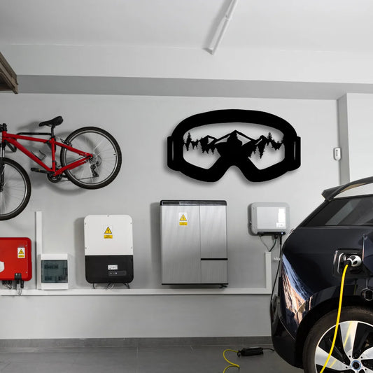 A large black metal mountain wall art piece shaped like ski goggles with mountain silhouettes creates a bold focal point above an electric car station.
