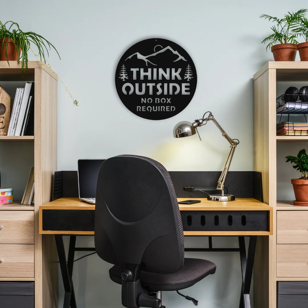 A round steel wall art with the quote “Think Outside – No Box Required” adds inspiration and edge to a modern workspace setup.
